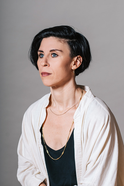 white person with black hair, blue eyes and brown lipstick gazing into the distance. 
